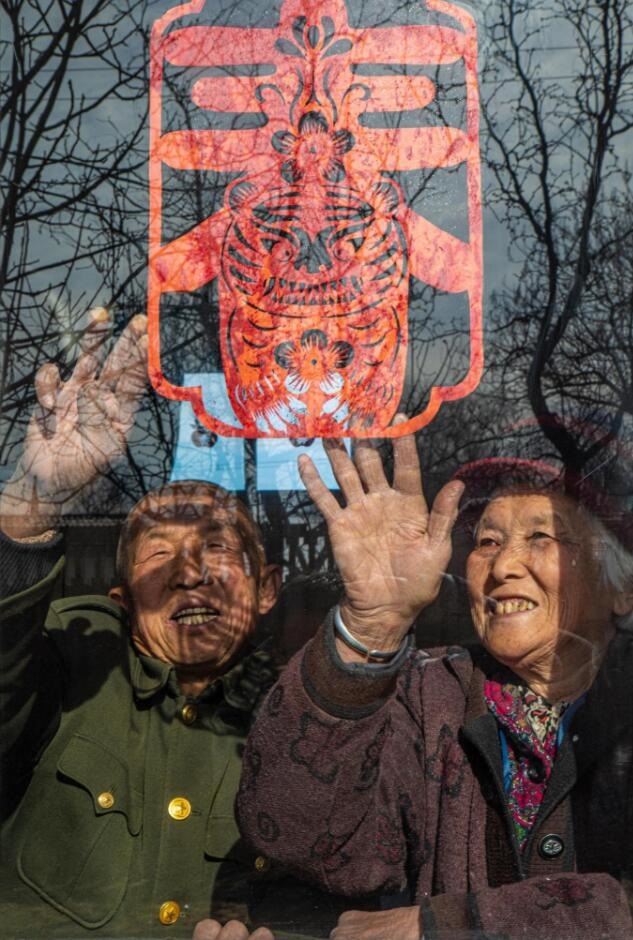 臘月里，霍州市師莊鄉(xiāng)馮南垣村村民師榮光(左)在災(zāi)后重建的新家里貼窗花。(霍州市委宣傳部供圖)