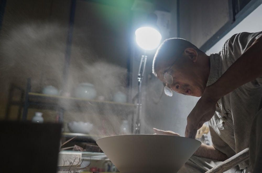 ↑ 在景德鎮(zhèn)，手工匠人吹去坯內(nèi)的泥土（2021年7月14日攝）。