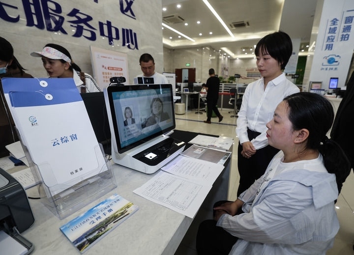 在浙江省嘉興市秀洲區(qū)王江涇鎮(zhèn)便民服務(wù)中心的“跨域通辦·云綜窗”窗口，辦理開業(yè)登記的個(gè)體工商戶（右一）通過該系統(tǒng)與江蘇省蘇州市吳江區(qū)盛澤鎮(zhèn)行政審批局工作人員視頻連線，進(jìn)行身份讀取及材料線上審核（2024年5月9日攝）。新華社記者 徐昱 攝
