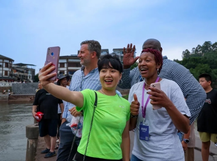 2024“一帶一路”媒體合作論壇聯(lián)合采訪調(diào)研行成員在樂山蘇稽古鎮(zhèn)與游客合影留念。本報記者 伊霄攝